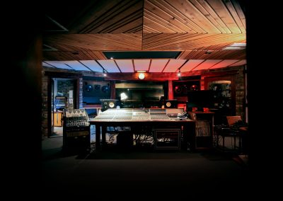 Wide view of a professional recording studio control room with a large mixing console, speakers, and equipment racks.