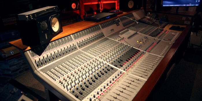 Wide view of a professional recording studio control room with a large mixing console, speakers, and equipment racks.